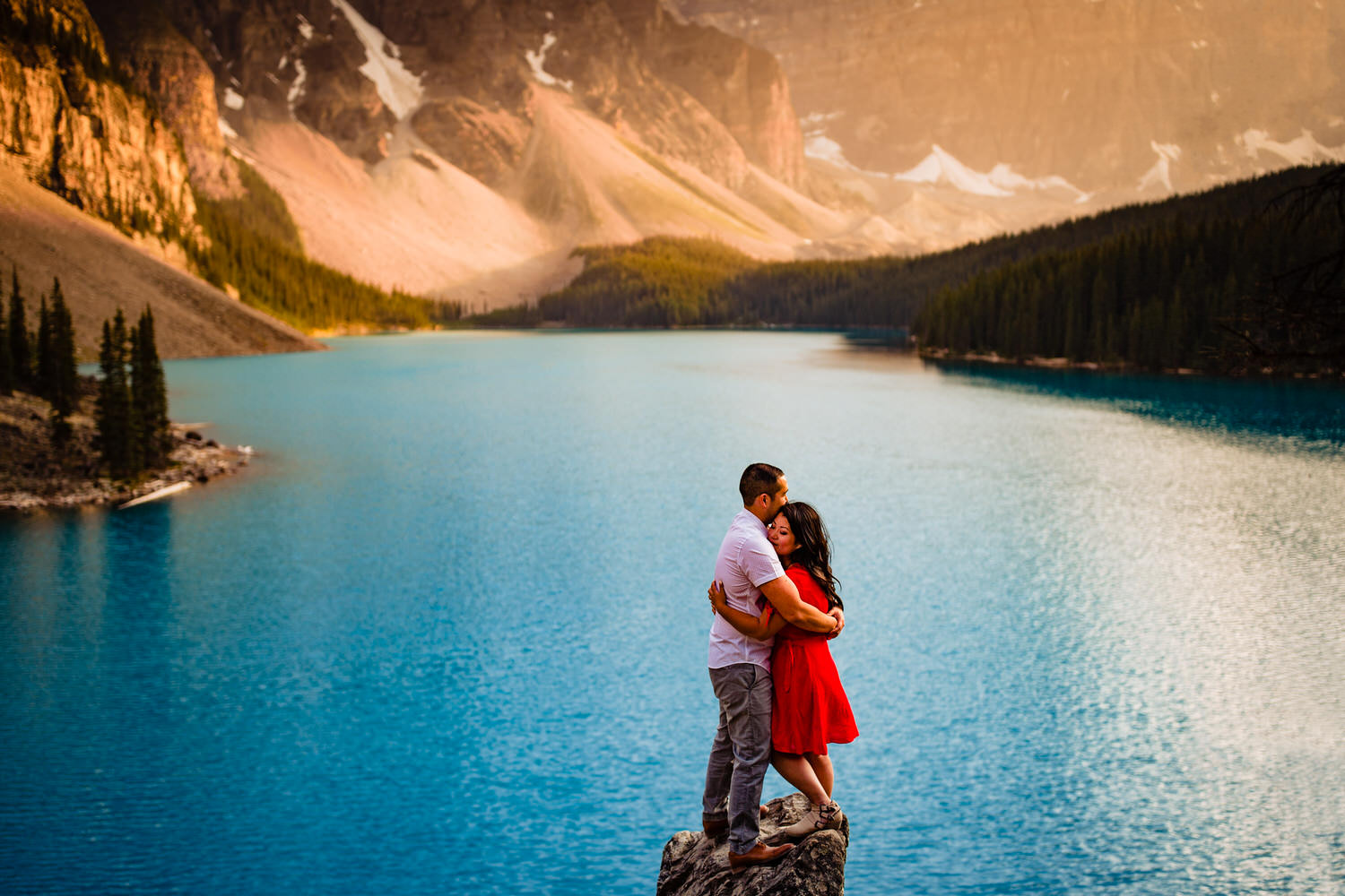 An engaged couple hugging on a rock located at Moraine Lake