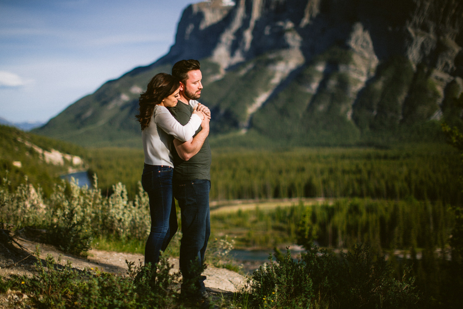 A photo of an engaged couple hugging in Banff National Park with Mt Rundle behind them